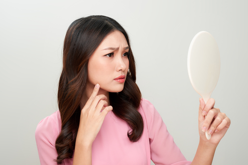 woman looking at the mirror with the trouble on her skin.